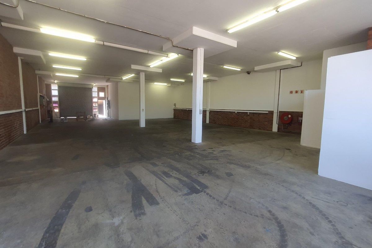 Spacious open-plan industrial unit featuring concrete flooring, exposed brick accents, structural columns, and functional fluorescent lighting throughout the expansive workspace.