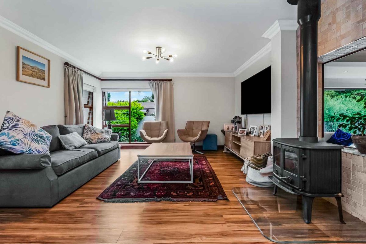 Spacious living room featuring warm wood-look flooring, a prominent cast-iron wood-burning stove, and large windows providing natural light and garden views.