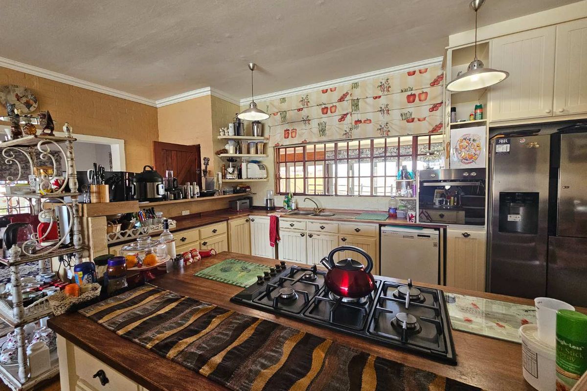 A rustic-style kitchen featuring a central island with a gas hob, timber countertops, built-in cabinetry, and a double sink with a window view.