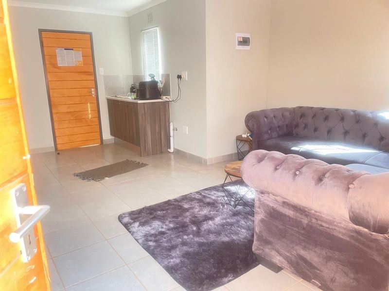 Open plan living area featuring tiled flooring, a compact kitchenette with built-in cabinetry, and a solid timber entrance door.