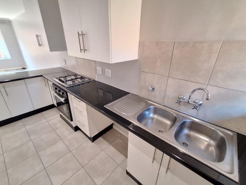 Modern kitchen featuring white cabinetry, black granite countertops, a gas hob, built-in oven, and a double stainless steel sink with tiled splashback.