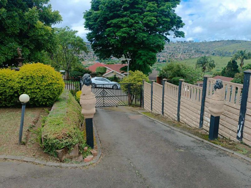 Front entrance view featuring an asphalt driveway, secure metal gate, and decorative stone pillars leading to the property.