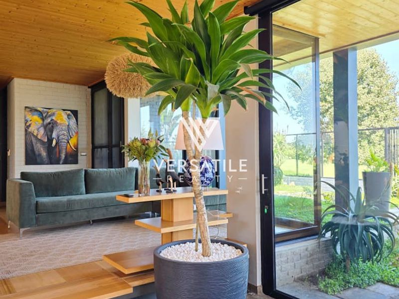 Modern living area featuring a warm timber ceiling, stone flooring, and large sliding glass doors that provide seamless access to the outdoor garden space.