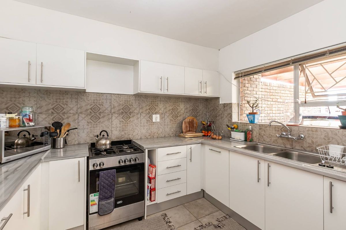 A functional kitchen featuring white cabinetry, patterned tile backsplash, stone-look countertops, a stainless steel gas stove, and a double basin sink.