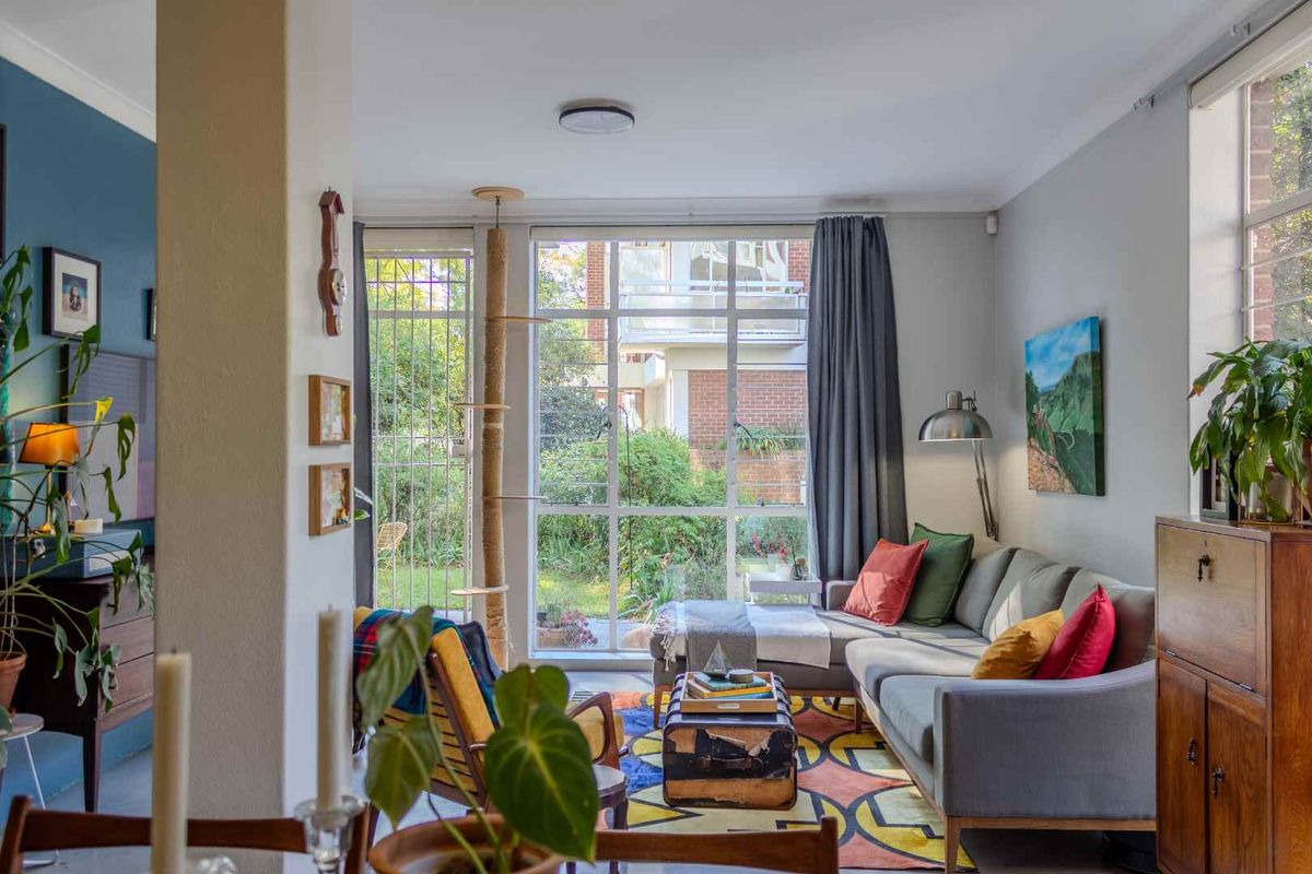 A bright living room featuring large floor-to-ceiling windows that provide ample natural light and a pleasant view of the garden area.