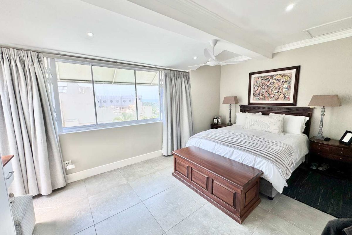A bright and spacious bedroom featuring large windows, neutral tiled flooring, recessed ceiling lighting, and a ceiling fan.