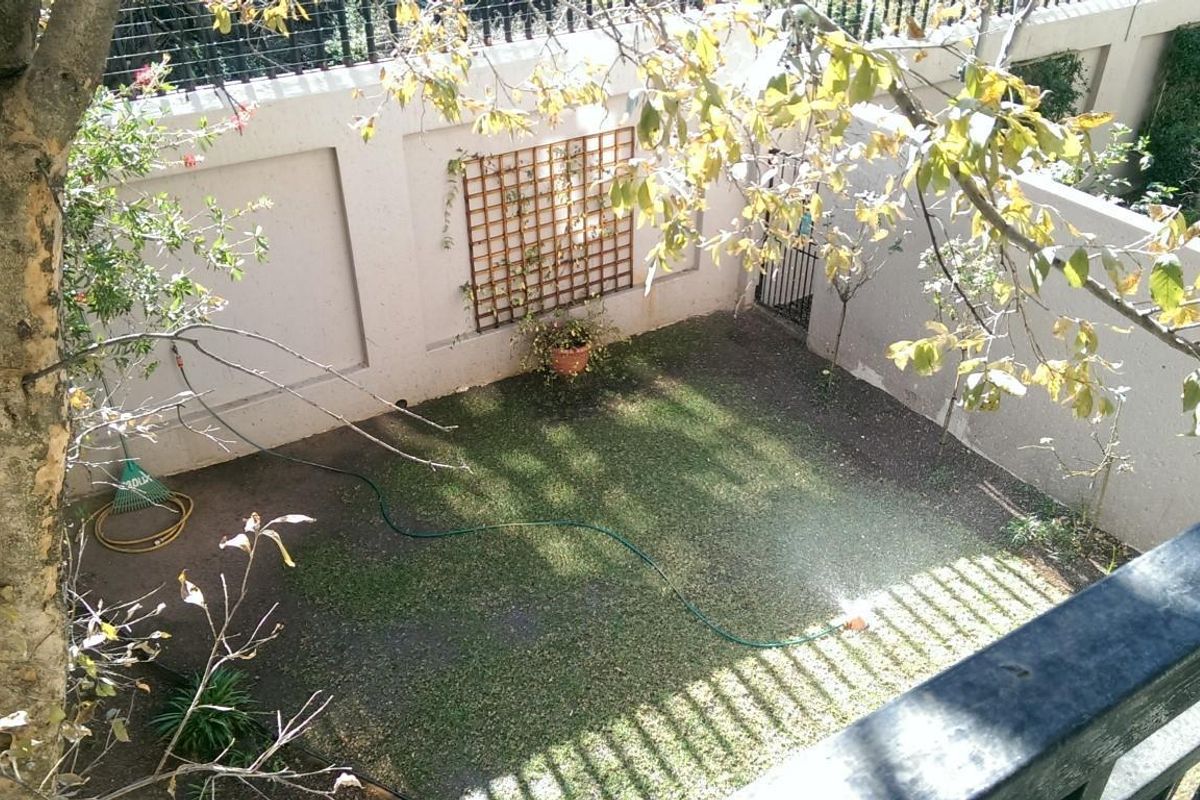 A private rear garden area featuring a lawn, perimeter wall with decorative trellis, and secure gated access.