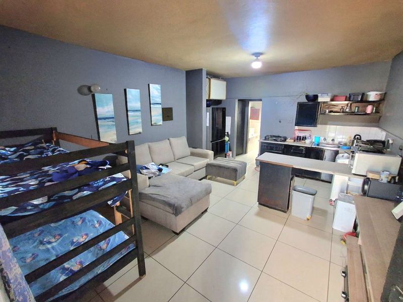 Open-plan living area featuring tiled flooring, a compact kitchen with built-in cabinetry, and a breakfast counter, suitable for versatile living arrangements.