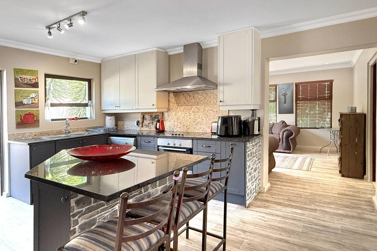 Modern kitchen featuring dark cabinetry, granite countertops, a central island with breakfast bar, stainless steel extractor fan, and mosaic tile backsplash.