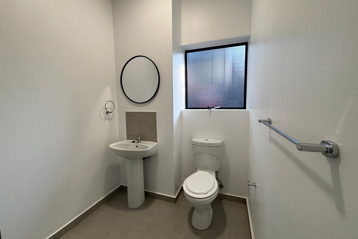 A clean and functional guest bathroom featuring a pedestal basin, toilet, and tiled flooring with a privacy window.