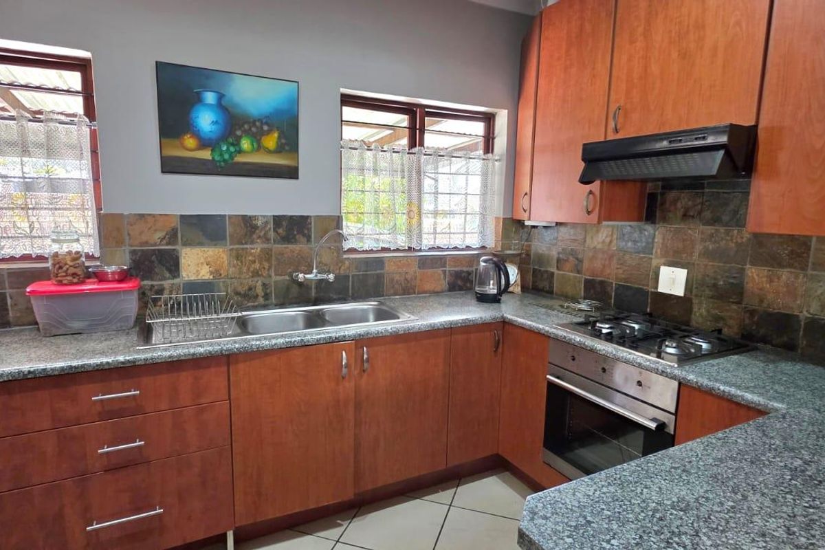 A functional kitchen featuring wood-finish cabinetry, granite countertops, a built-in oven with gas hob, and a decorative slate tile backsplash.