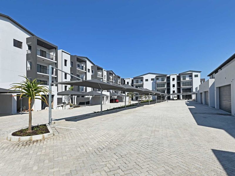 Exterior view of a modern apartment complex featuring paved parking areas, covered carports, and multi-story residential buildings with balconies.