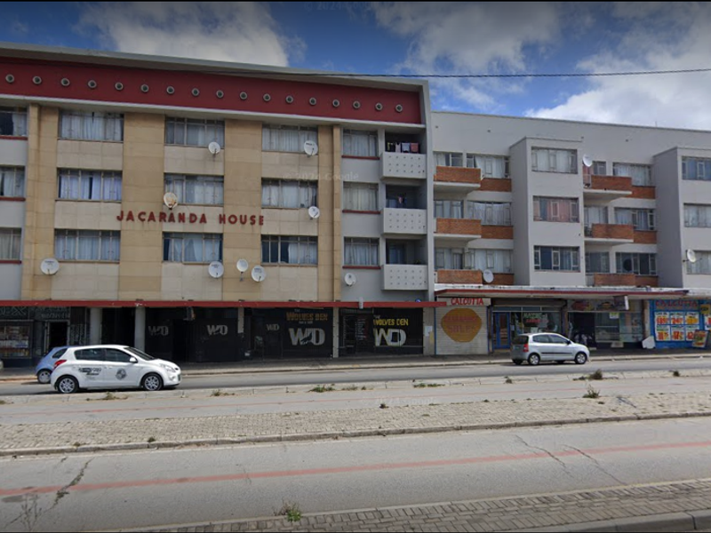 Street-facing view of Jacaranda House, a multi-story apartment building featuring ground-level retail spaces and residential balconies.