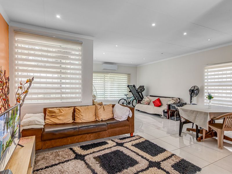 Spacious open-plan living area featuring tiled flooring, recessed downlighting, and a wall-mounted air conditioning unit.