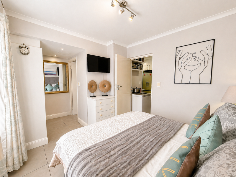 A well-maintained bedroom featuring tiled flooring, cove cornicing, and track lighting, with an adjacent built-in scullery or utility area.