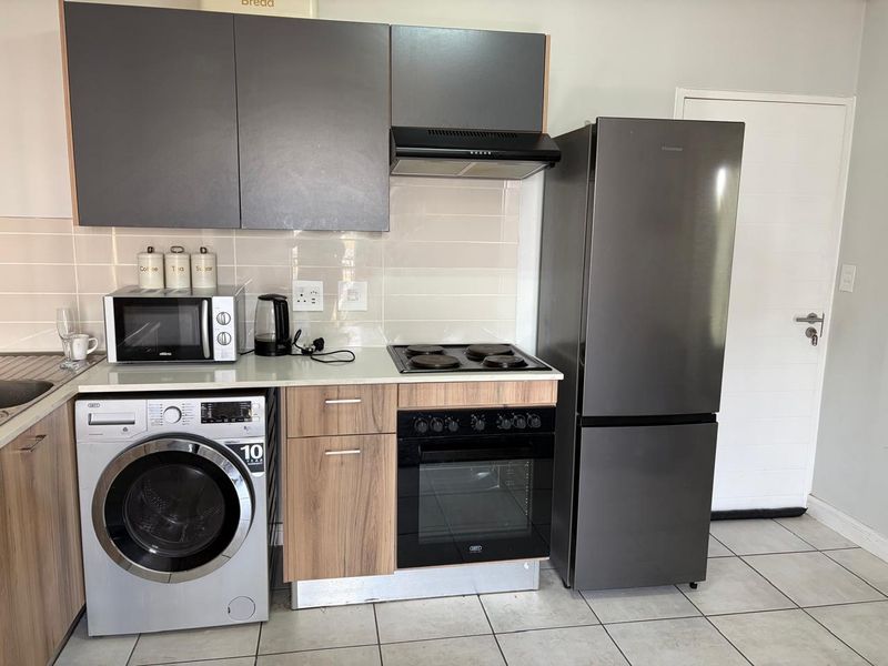 A functional kitchen featuring modern grey cabinetry, built-in oven and hob, extractor fan, tiled backsplash, and tiled flooring.