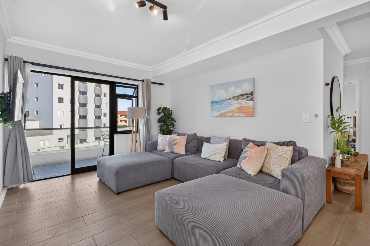A bright living room featuring wood-look tile flooring, crown molding, and a sliding glass door leading to a private balcony.