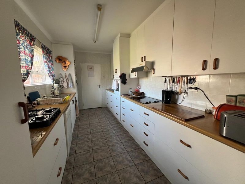 A functional galley-style kitchen featuring white cabinetry, laminate countertops, tiled flooring, and integrated appliances, offering a practical layout with potential for modern updates.