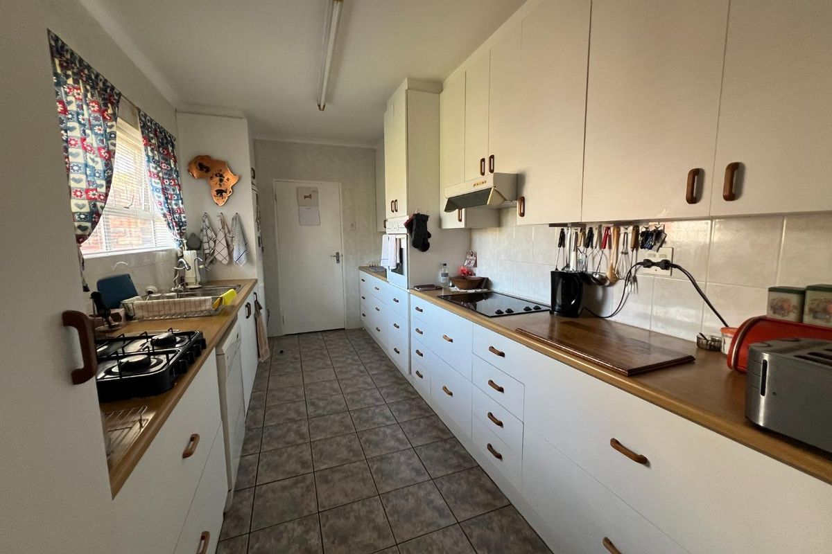 A functional galley-style kitchen featuring white cabinetry, laminate countertops, tiled flooring, and integrated appliances, offering a practical layout with potential for modern updates.