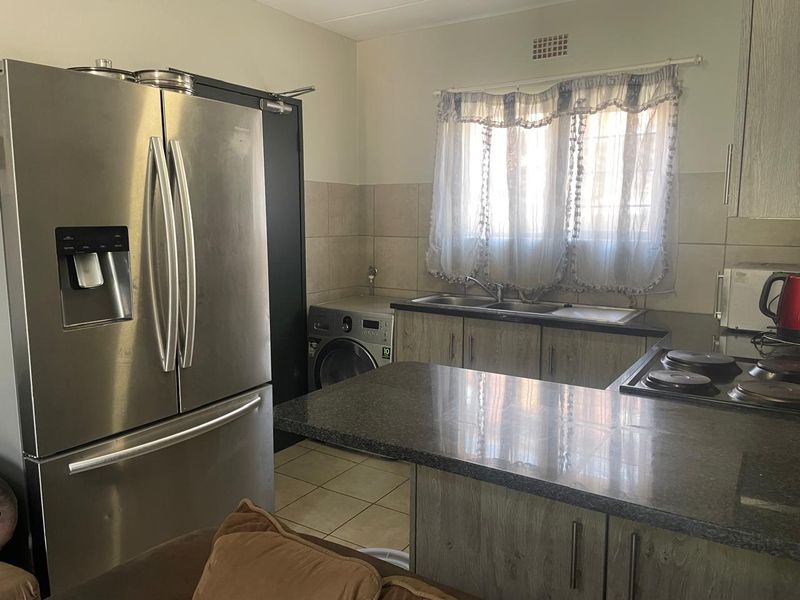 Functional kitchen featuring wood-look cabinetry, granite countertops, a double basin sink, and a built-in hob with tiled finishes.