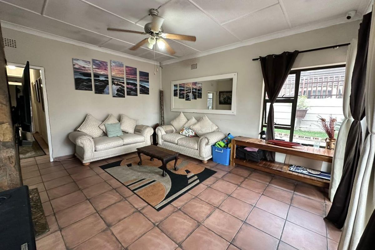 A spacious living room featuring tiled flooring, a ceiling fan, and large windows that provide natural light and access to the exterior.