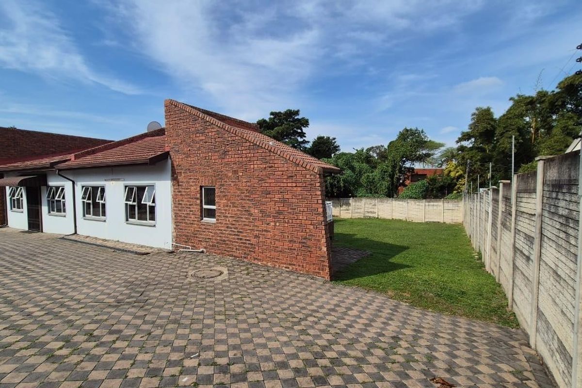 Rear view of the property featuring a brick facade, tiled roof, paved driveway, and a private lawn enclosed by a precast concrete boundary wall.