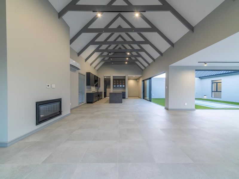 Spacious open-plan living area featuring a vaulted ceiling with exposed trusses, modern kitchen, built-in fireplace, and seamless access to the outdoor patio and pool area.