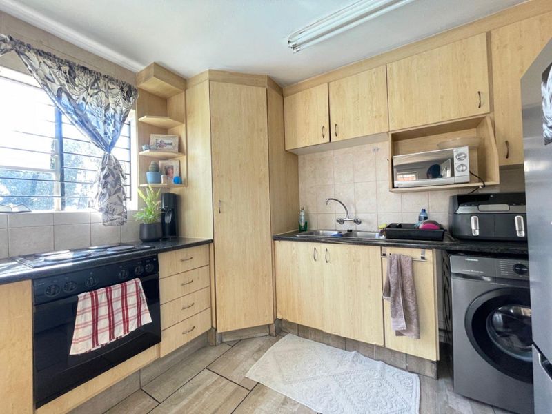 Functional kitchen featuring light wood-finish cabinetry, tiled backsplash, built-in oven and hob, and tiled flooring with security bars on the window.