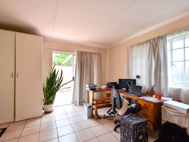 A functional home office featuring tiled flooring, a built-in wardrobe, and direct access to an outdoor patio area through a sliding glass door.