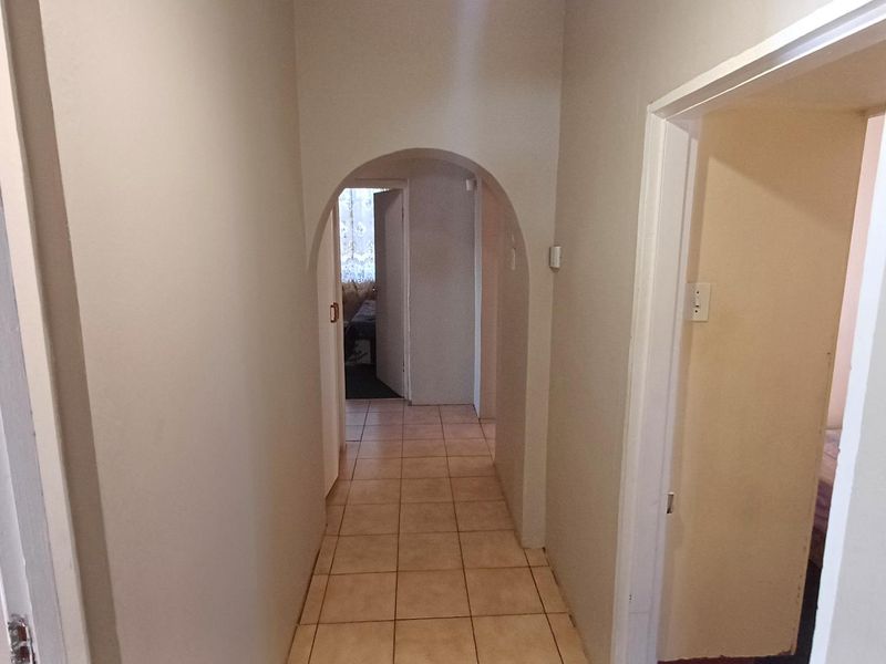 A clean, neutral-toned hallway featuring tiled flooring and a distinctive arched architectural detail leading to adjacent rooms.