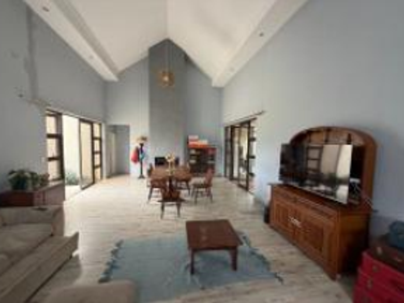 Spacious open-plan living and dining area featuring a high vaulted ceiling, central fireplace, and large sliding glass doors leading to the exterior.