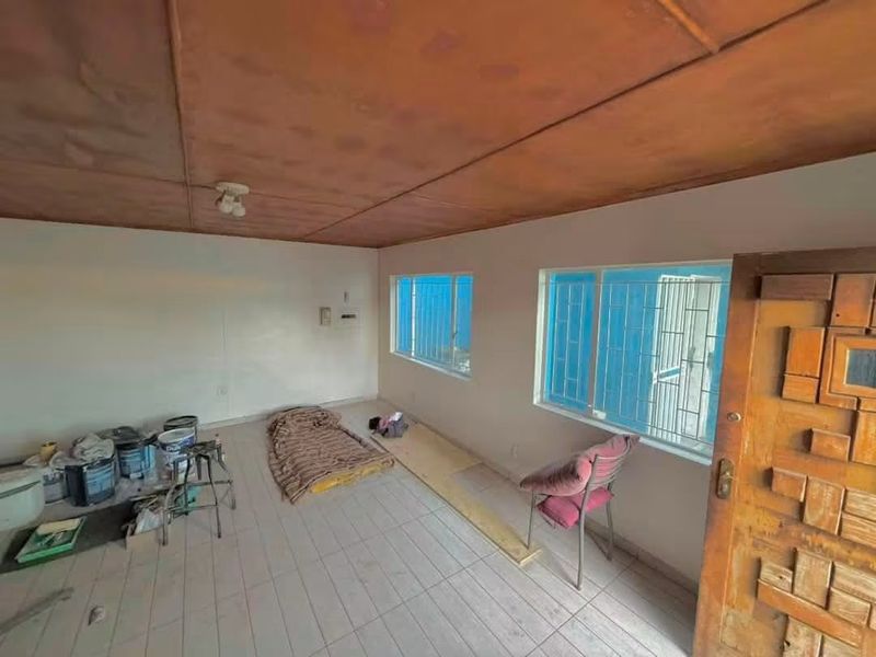 An empty living area featuring tiled floors, security-barred windows, and a timber panel ceiling, currently undergoing minor maintenance.