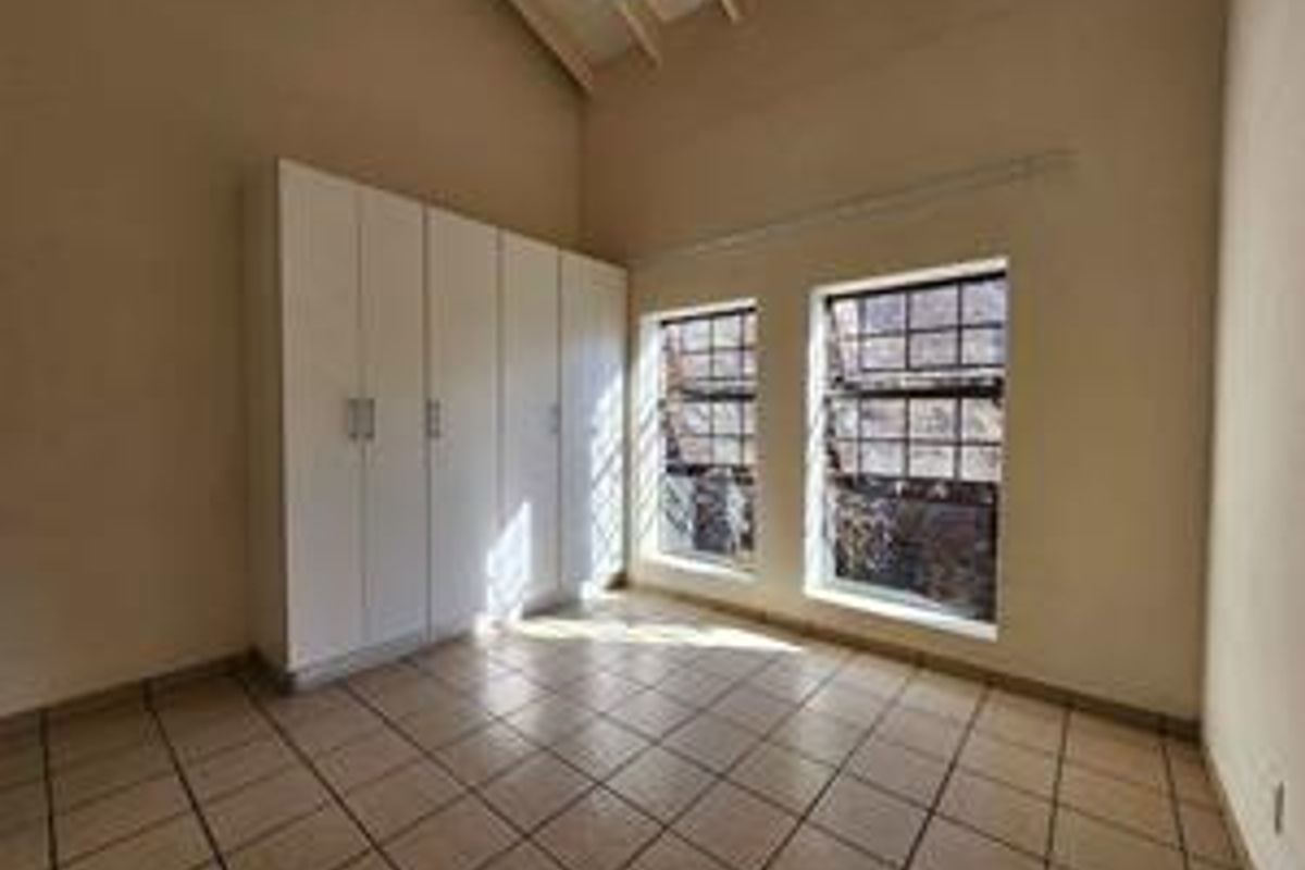 A bright, empty bedroom featuring tiled flooring, vaulted ceilings, and built-in cupboards, offering a clean canvas for personalization.