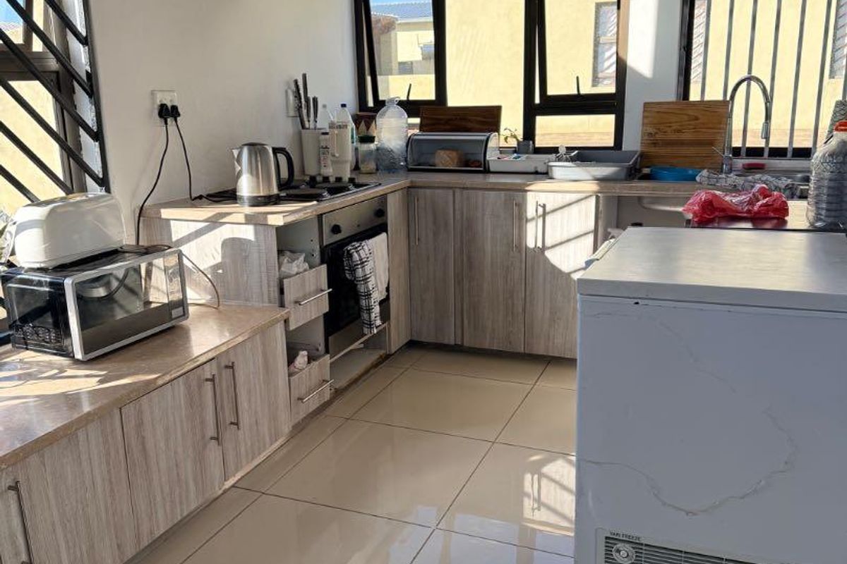 A functional kitchen featuring light wood-grain cabinetry, tiled flooring, built-in oven, extractor fan, and large windows providing ample natural light.