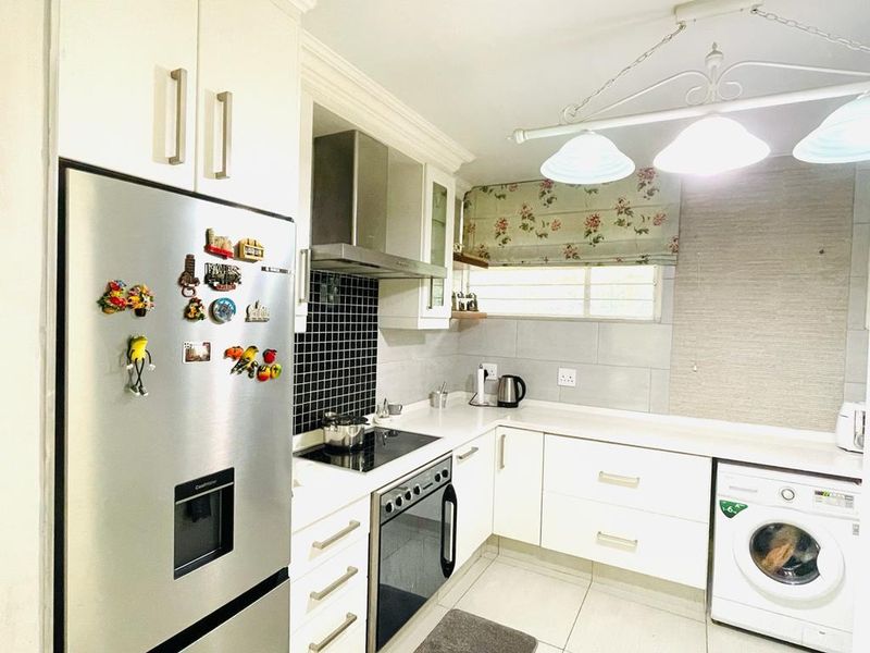 A functional kitchen featuring white cabinetry, stone countertops, a black tiled backsplash, and built-in appliances including an oven, hob, and extractor fan.