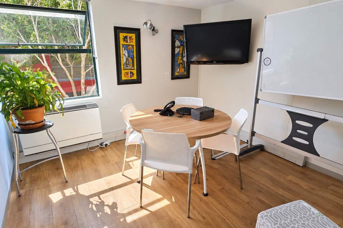 A functional office space featuring laminate flooring, a wall-mounted heater, and a large window providing natural light.