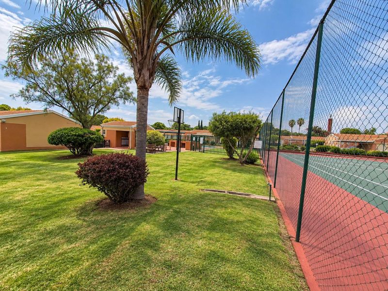 Communal sports facility featuring a fenced tennis court and basketball hoop set within a well-maintained landscaped garden area.