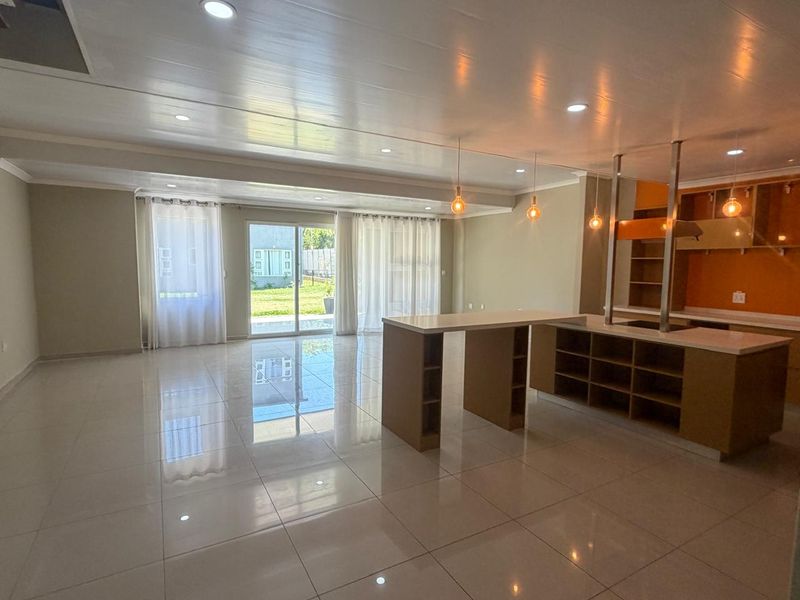 Spacious open-plan living and kitchen area featuring polished tile flooring, modern cabinetry, a central island, and large sliding doors leading to the garden.