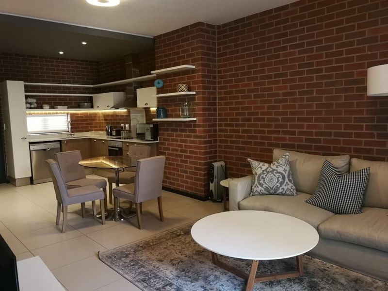 Modern open-plan living area featuring an exposed brick feature wall, tiled flooring, and a well-appointed kitchen with built-in cabinetry and integrated appliances.