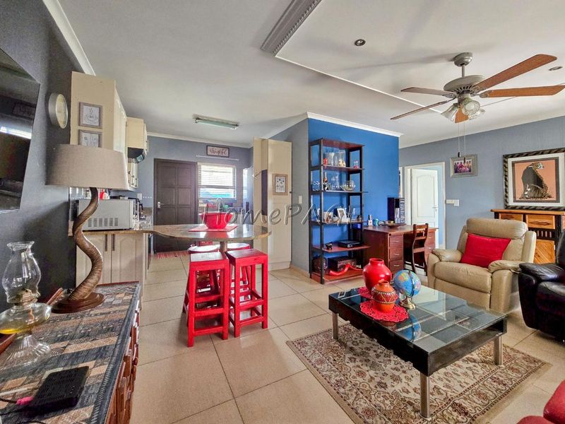 Open-plan living area featuring tiled flooring, a breakfast counter, kitchen cabinetry, and a ceiling fan, creating a functional combined kitchen and lounge space.