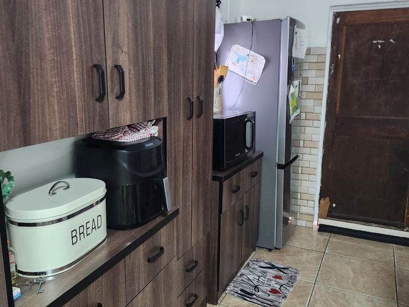 A functional kitchen featuring dark wood-grain cabinetry, tiled flooring, and a tiled backsplash, with direct access to an exterior door.