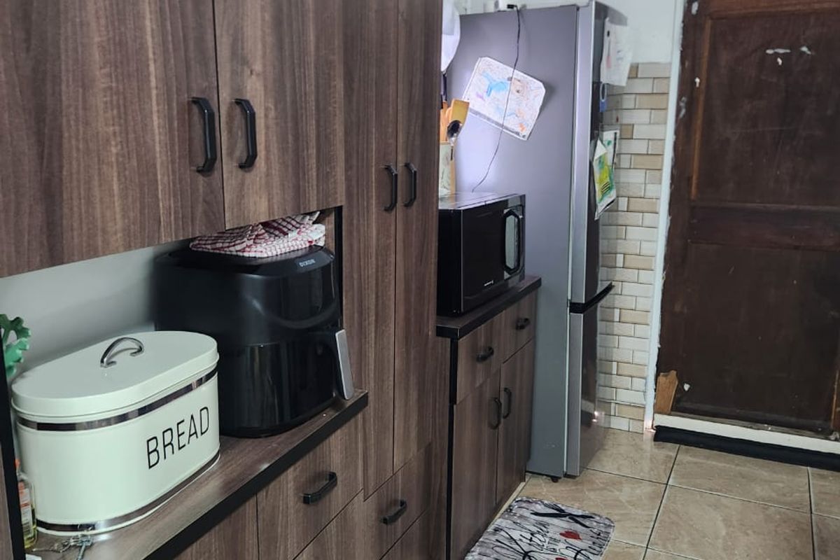 A functional kitchen featuring dark wood-grain cabinetry, tiled flooring, and a tiled backsplash, with direct access to an exterior door.
