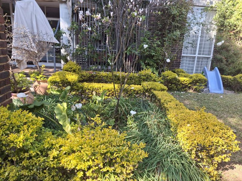 A private garden area featuring landscaped hedges, established plants, and direct access to the apartment via sliding glass doors with security bars.