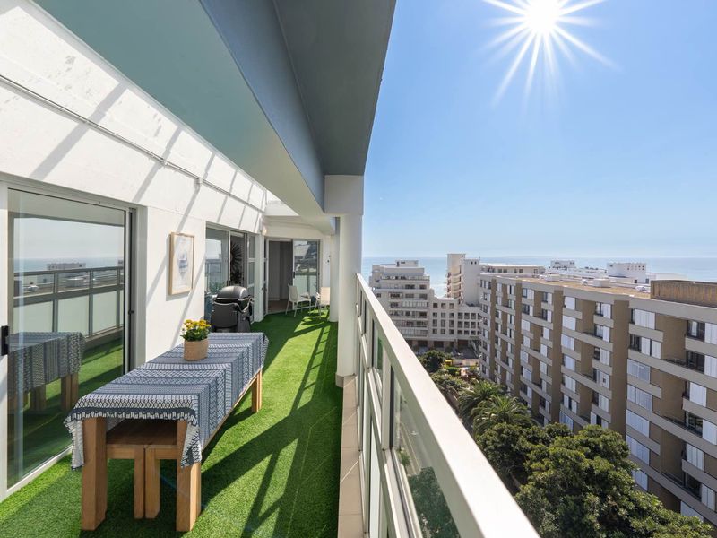 Spacious covered balcony featuring a glass balustrade, artificial turf flooring, and direct access to the apartment through large sliding glass doors.