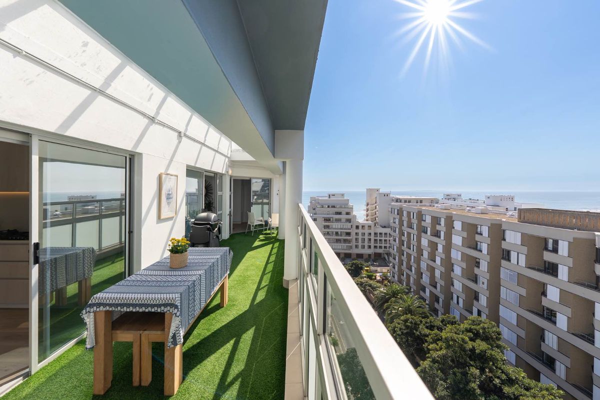 Spacious covered balcony featuring a glass balustrade, artificial turf flooring, and direct access to the apartment through large sliding glass doors.