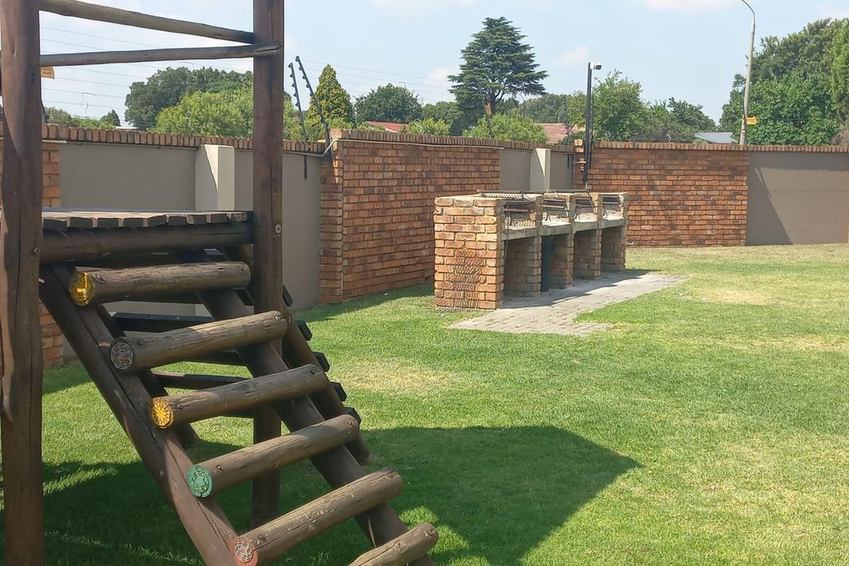 A spacious rear garden featuring a built-in brick braai area, enclosed by a secure brick boundary wall with electric fencing.