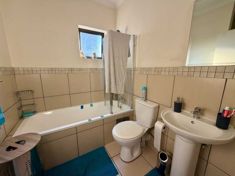 A functional bathroom featuring a bathtub with a glass screen, pedestal basin, and toilet, finished with neutral wall and floor tiling.
