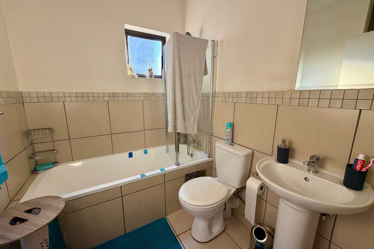 A functional bathroom featuring a bathtub with a glass screen, pedestal basin, and toilet, finished with neutral wall and floor tiling.