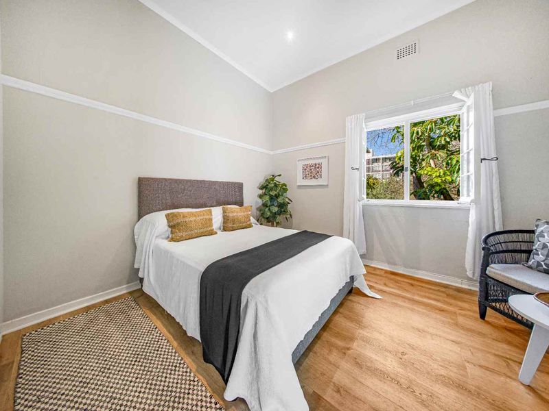 A bright and well-maintained bedroom featuring timber flooring, classic picture rails, and a casement window overlooking greenery.