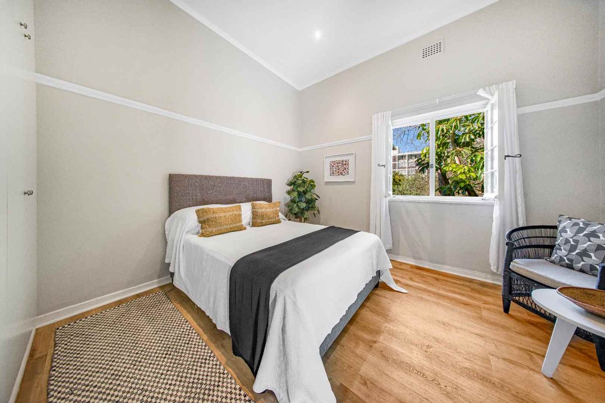 A bright and well-maintained bedroom featuring timber flooring, classic picture rails, and a casement window overlooking greenery.